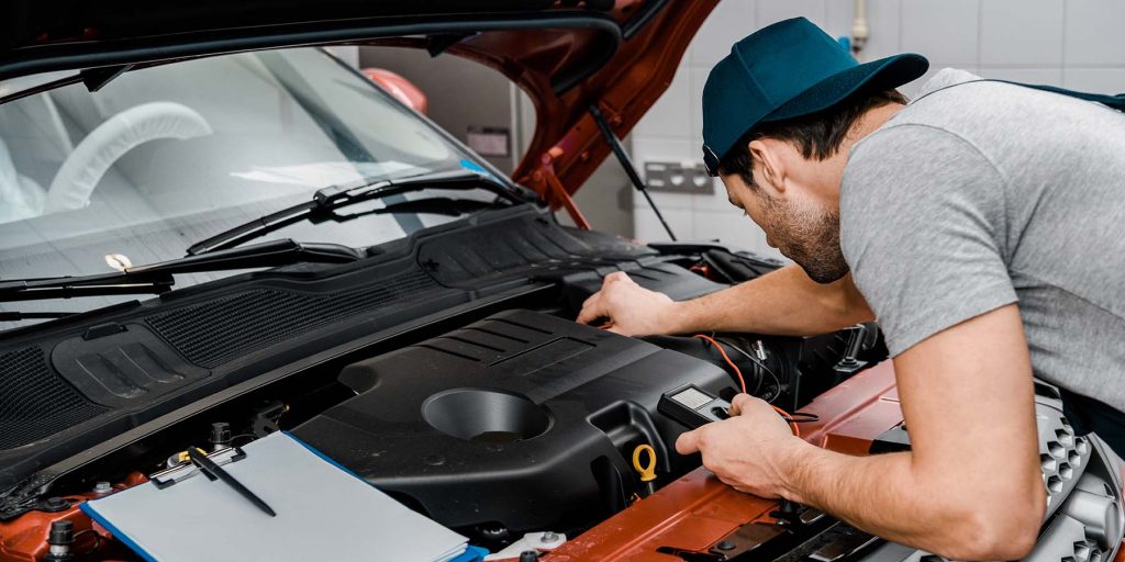 auto mechanic with multimeter voltmeter checking car battery voltage at mechanic shop