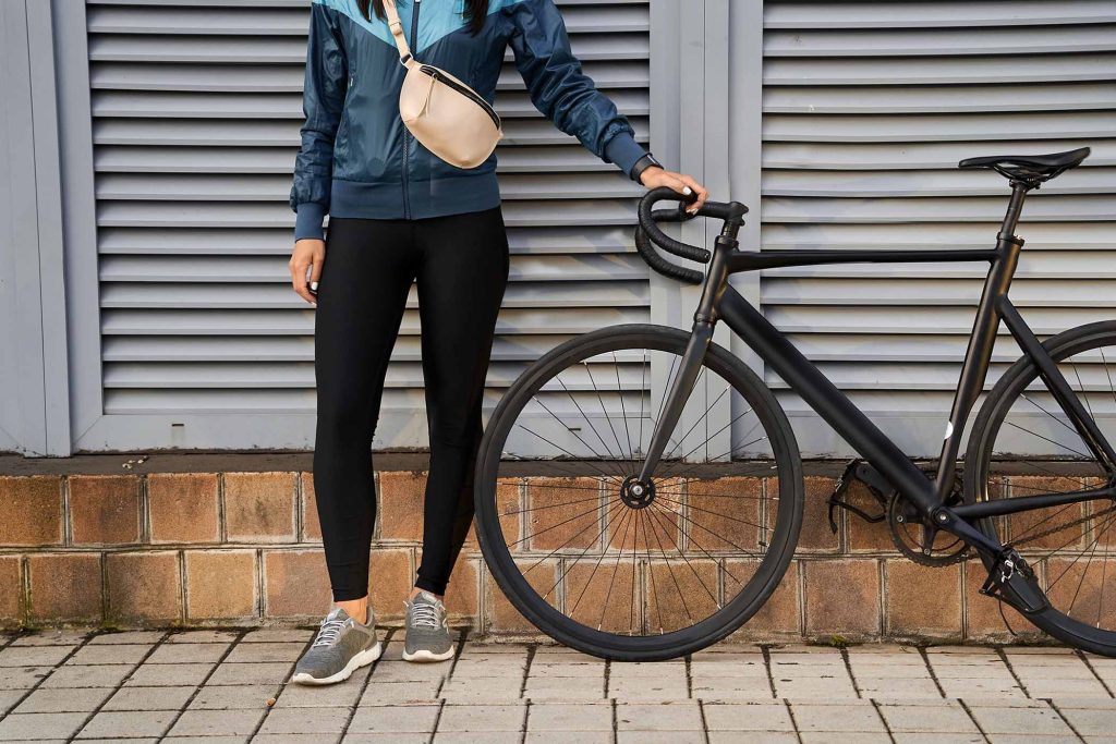 Cropped photo of young woman in sportswear standing near the bike on the street. Sport and lifestyle concept