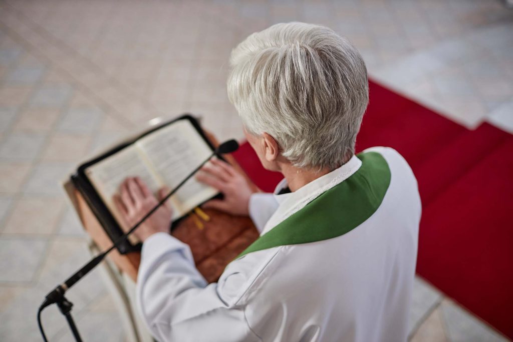 High angle view of senior priest reading Bible in microphone standing behind the altar in church