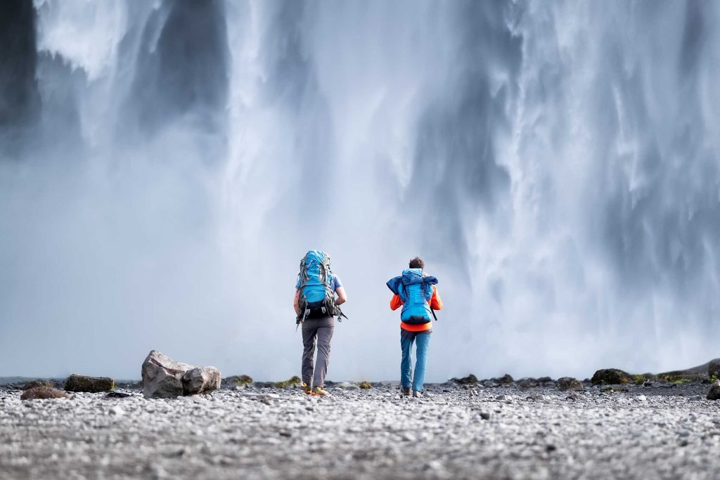 Travelers couple look at the Skogafoss waterfall. Travel and active life concept with team. Adventure and travel in the Iceland.