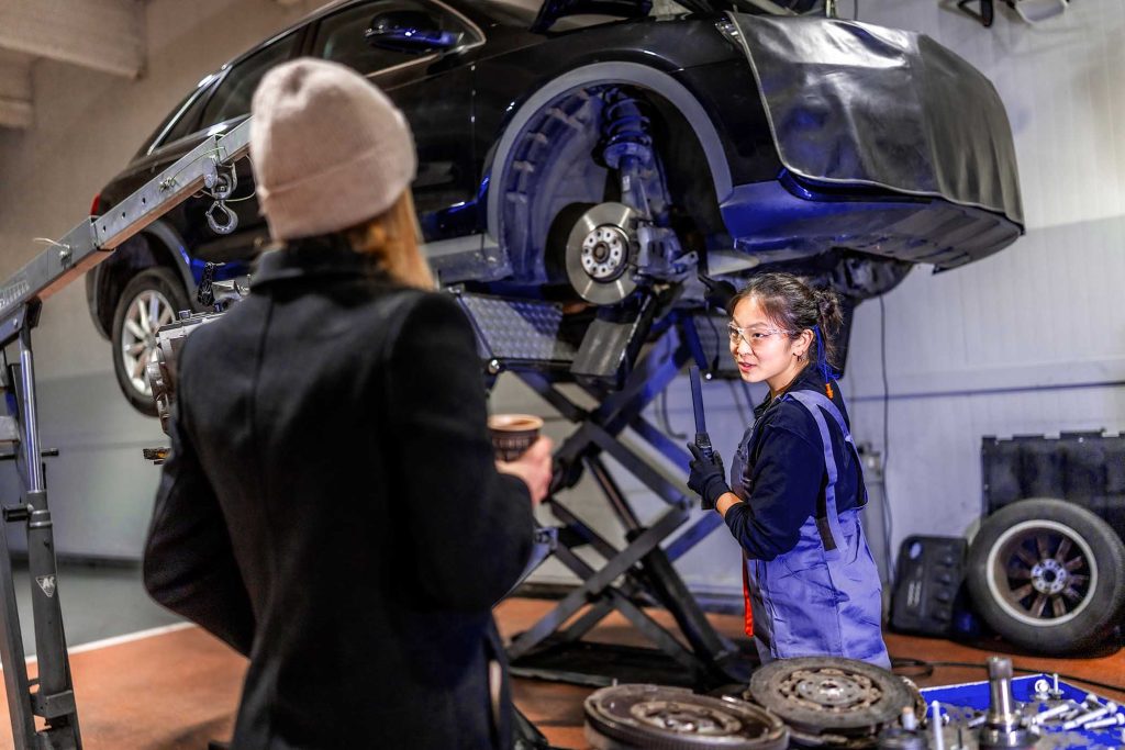Professional female mechanic explaining car repair processes to a customer in a busy auto repair shop, fostering trust and satisfaction