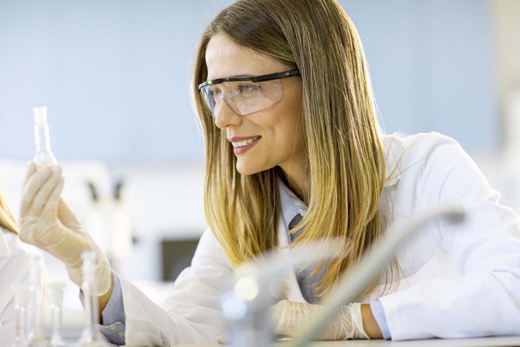 Young female medical or scientific researcher looking at a flasks with solutions in a laboratory