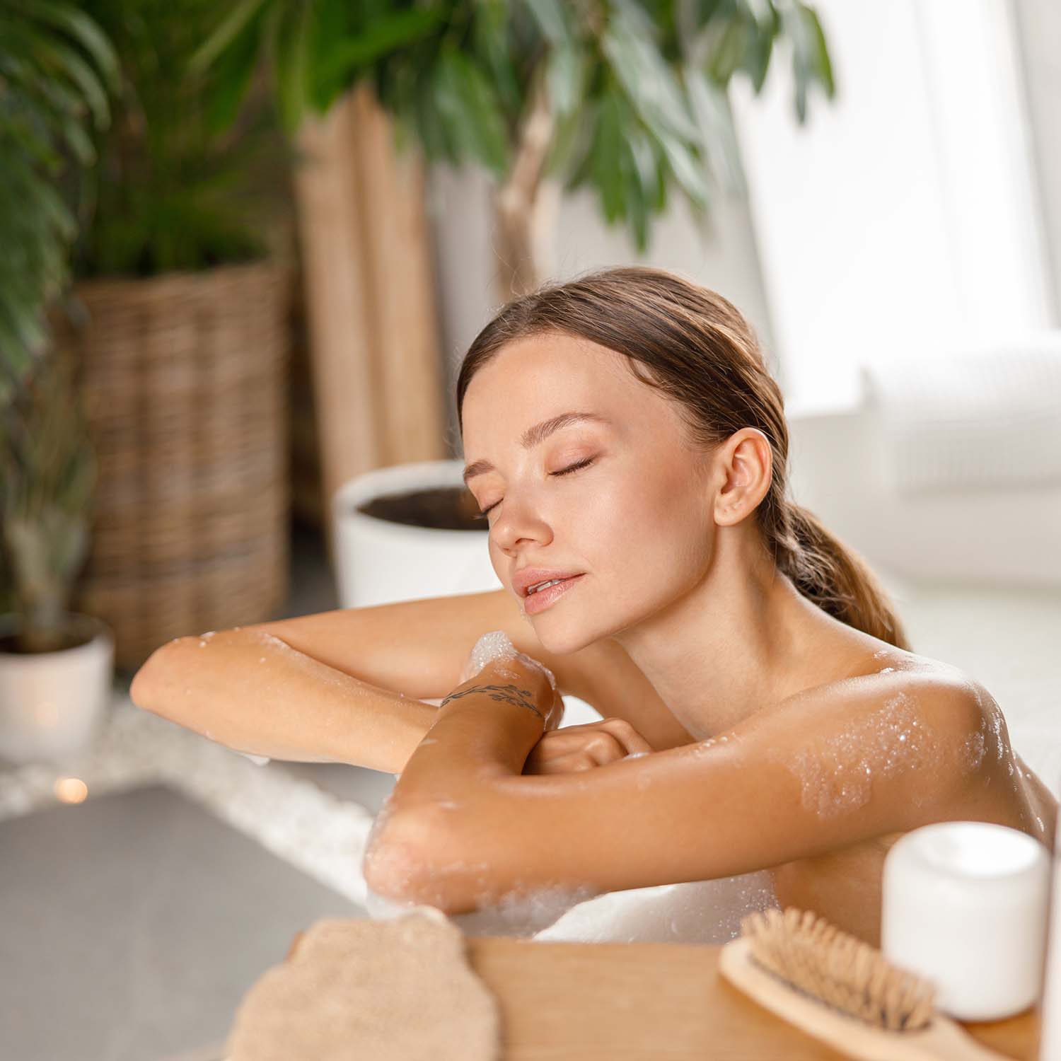 Relaxed young woman leaning on bathtub side while bathing with eyes closed at spa resort. Wellness, beauty and care concept