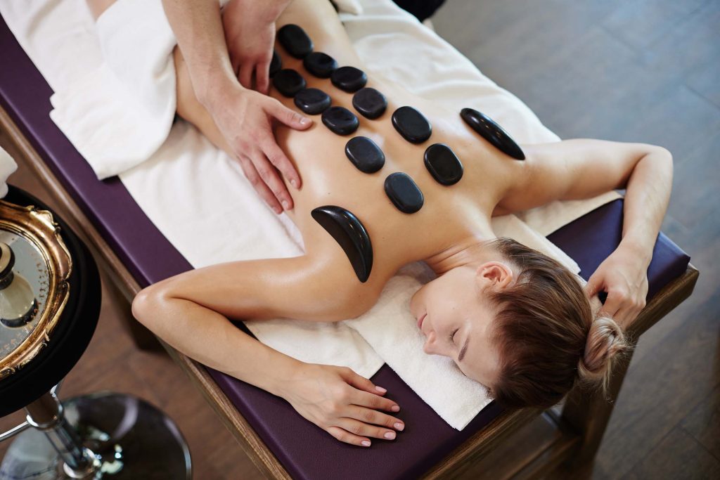 High angle portrait of young woman enjoying stone therapy lying on massage table in SPA center