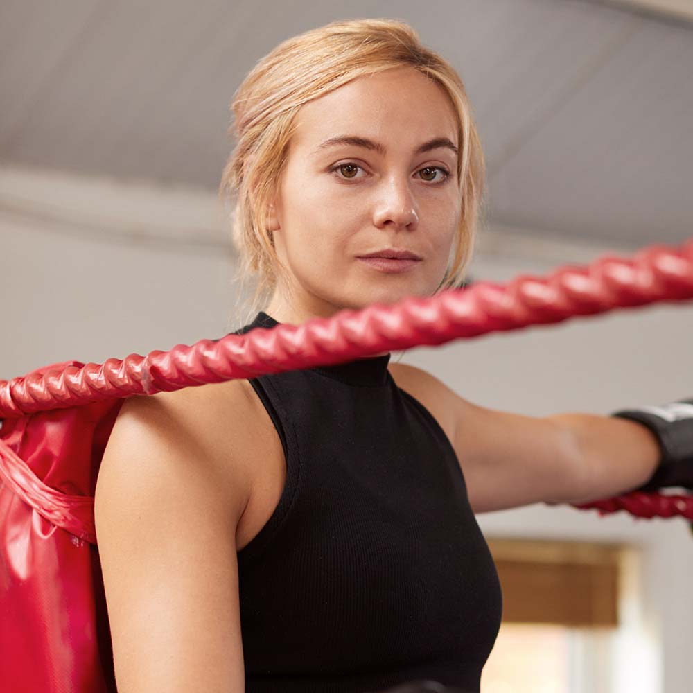Portrait Of Female Boxer In Gym Wearing Boxing Gloves Standing In Boxing Ring