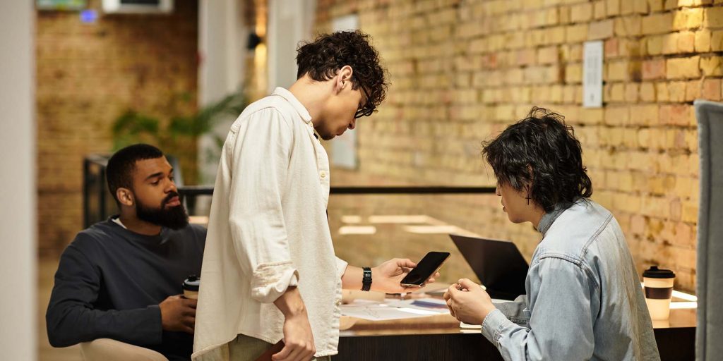 Three people discuss ideas and technology around a table in an office.