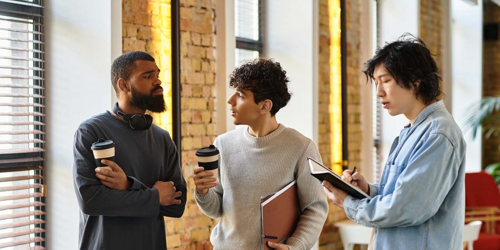 In a bright workspace, three coworkers share coffee and enthusiastically exchange ideas.