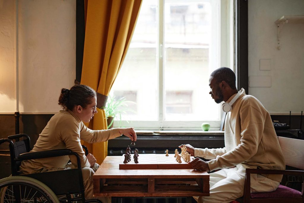 African man playing chess together with his friend with disability, they sitting in the room