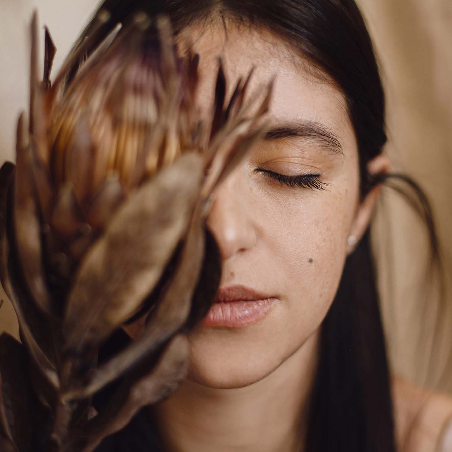 A woman holding a protea flower near her face during a skin consultation