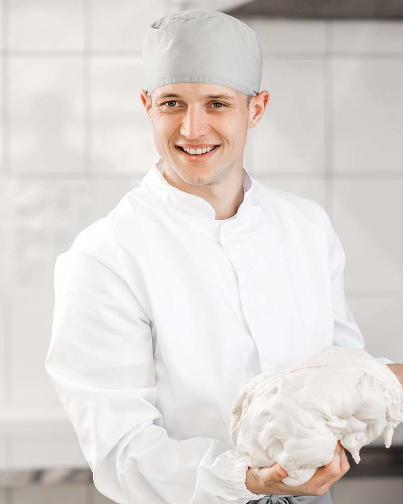 Portrait of a male baker mixing dough with professional kneader machine at the manufacturing
