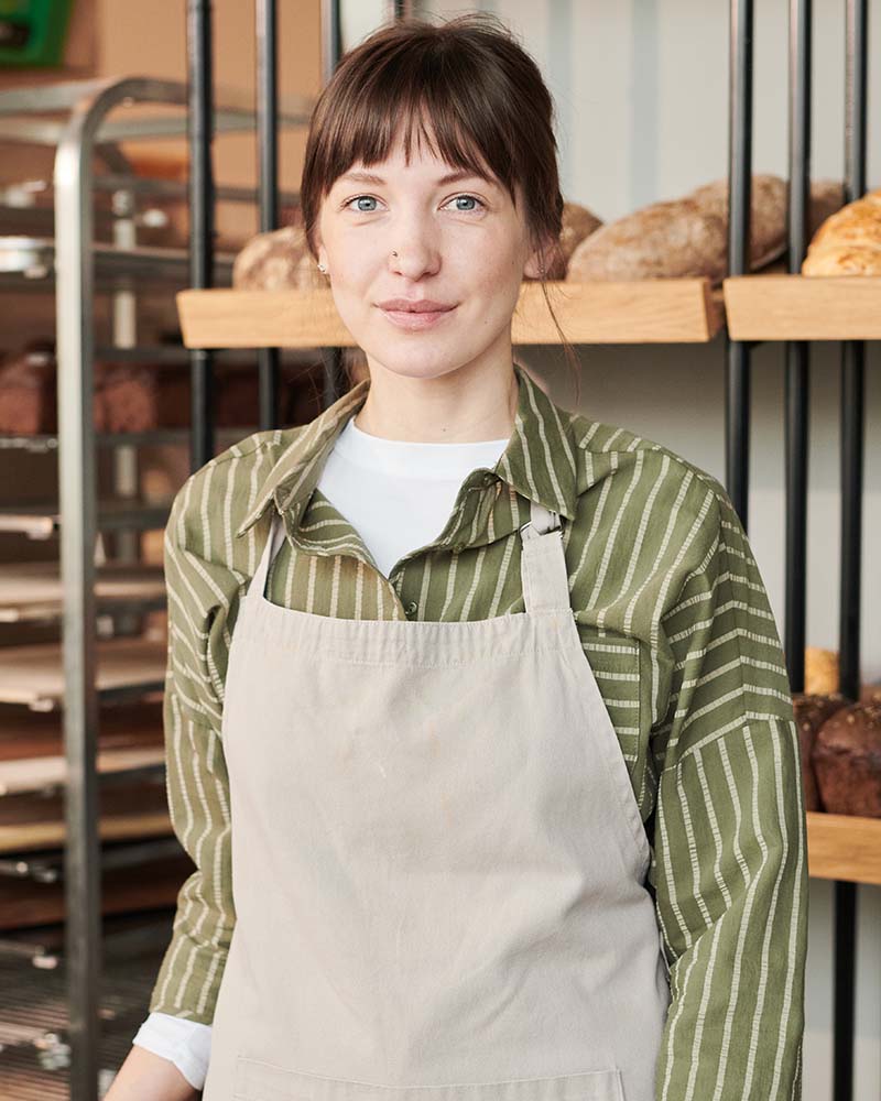 Portrait of young woman in apron looking at camera while standing in bakery