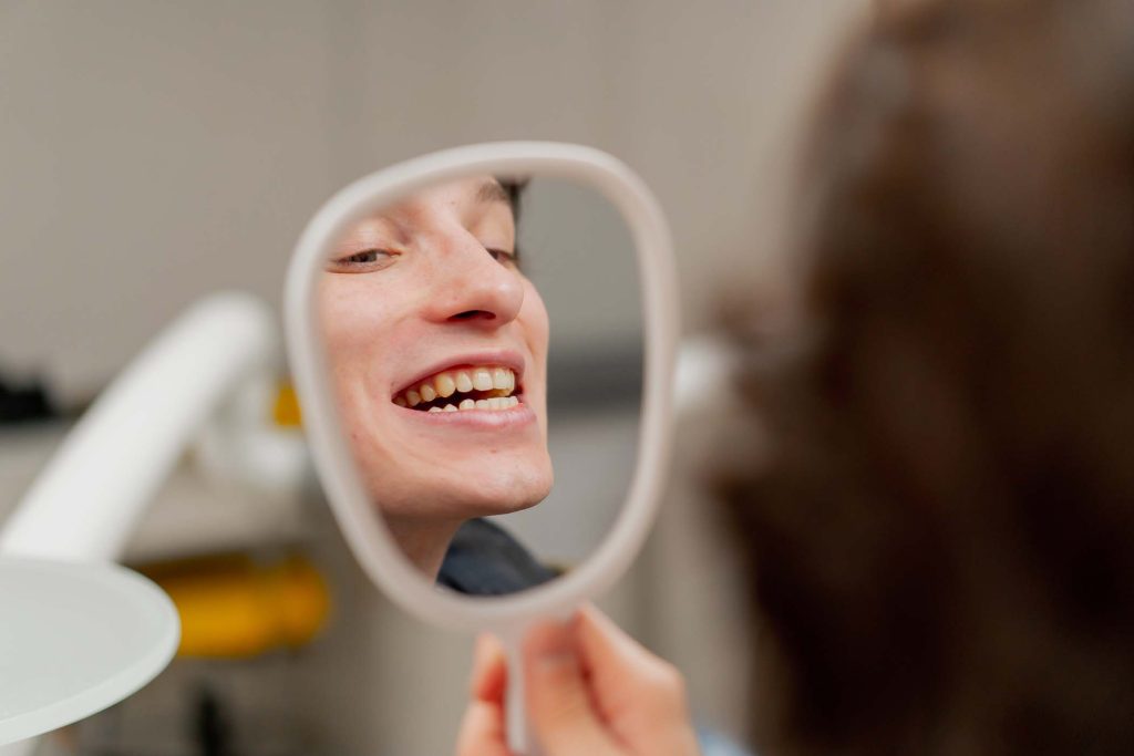 close up dental office a young guy sits in a chair and looks at his teeth through a dental mirror