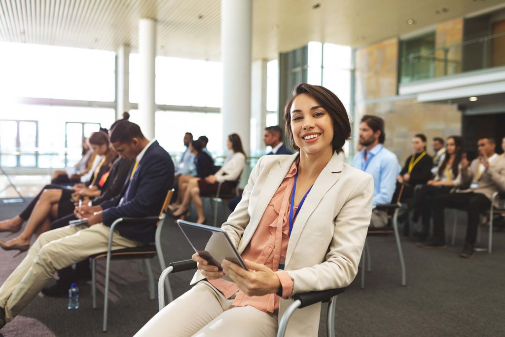 Front view of happy young mixed race businesswoman with digital tablet looking at camera during seminar in office building
