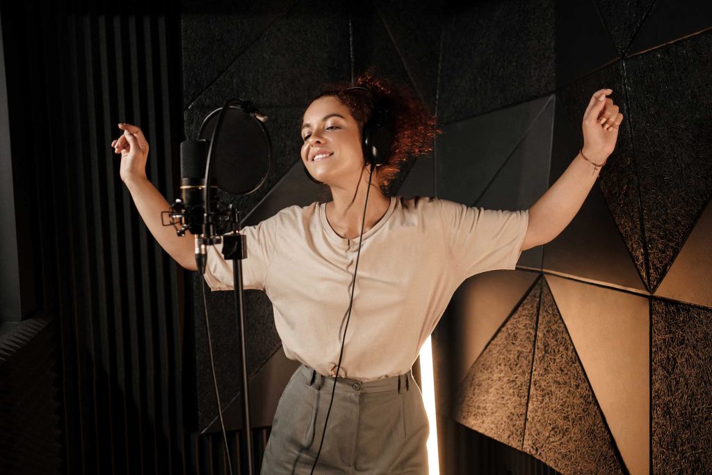 Beautiful female musician in headphones sensually dancing and singing in sound recording studio