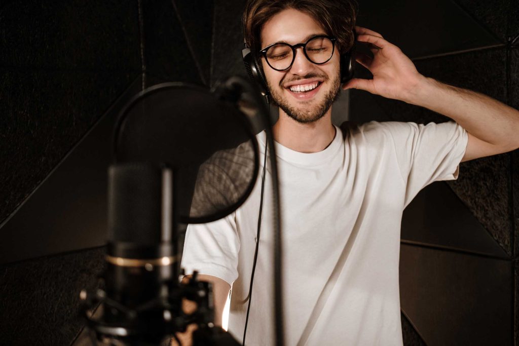 Young attractive male singer in headphones joyfully singing in modern sound studio