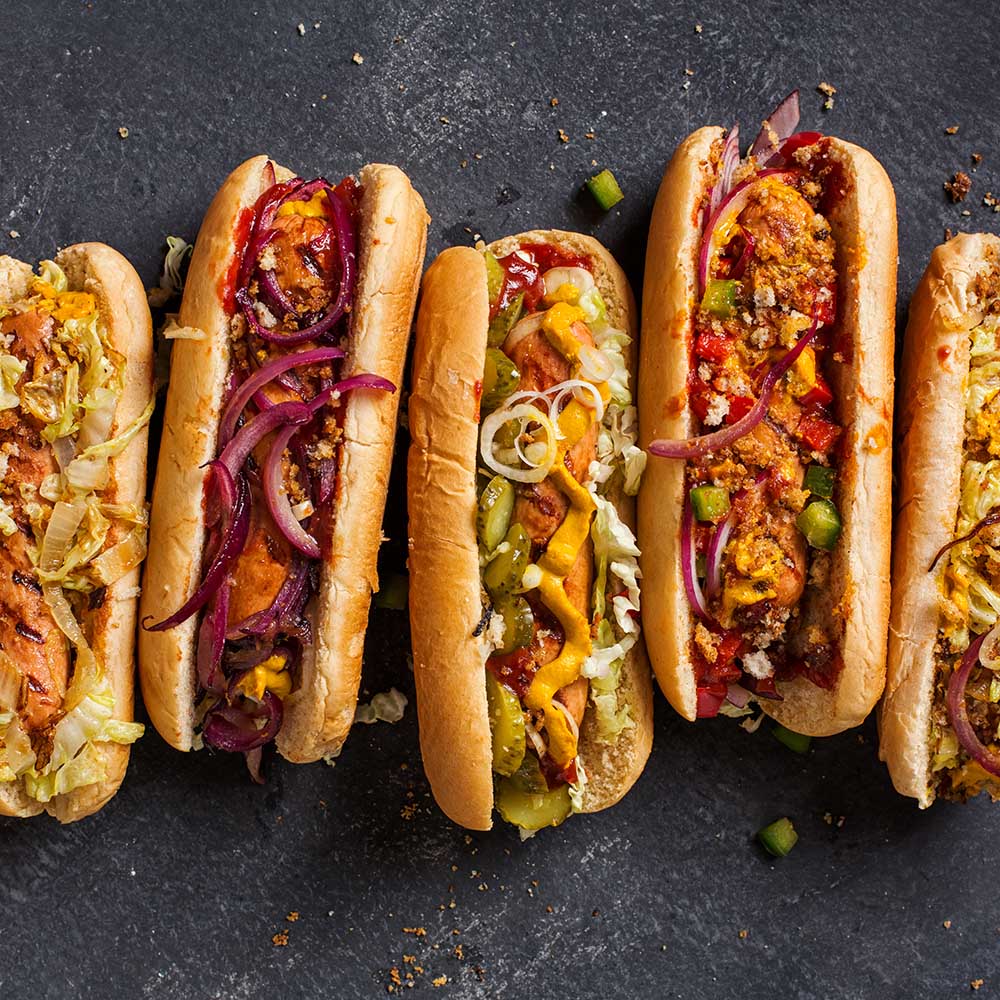 Hot dogs with a sausage on a fresh rolls garnished with mustard and ketchup and served with different toppings.