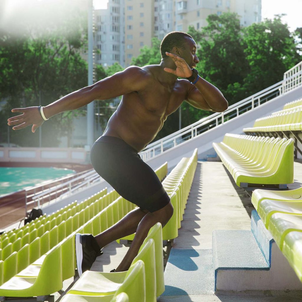 Side view of a muscular healthy african man athlete running upstairs at the stadium