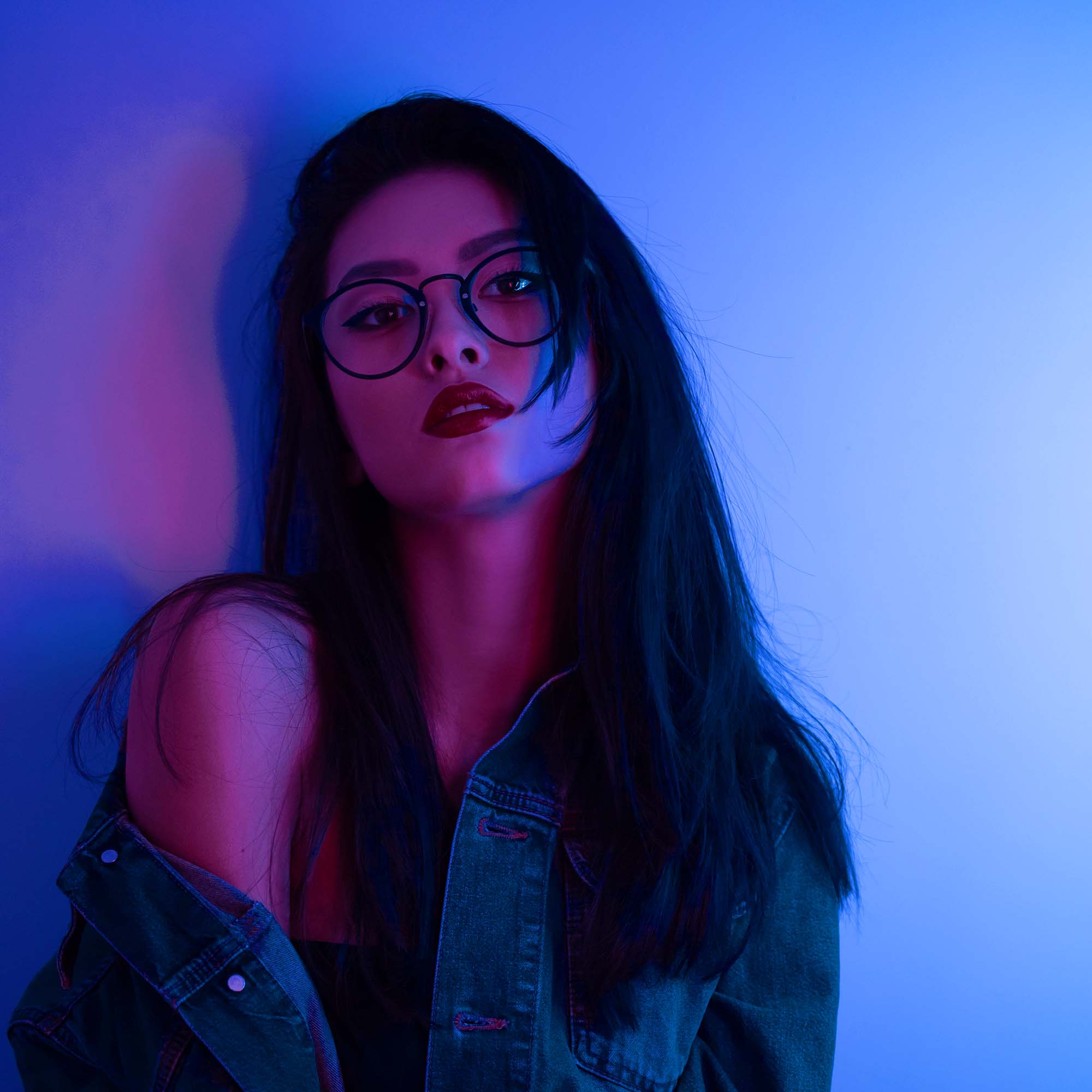 Fashion portrait of young elegant woman. Young asian millennial girl in fashion style wearing glasses casual clothes, neon light blue background, night life and fashion lifestyle.