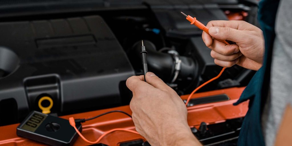 cropped shot of auto mechanic with multimeter voltmeter checking car battery voltage at mechanic