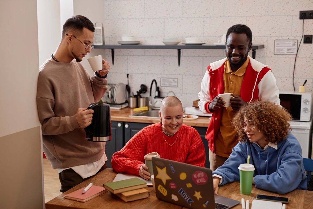 Multiethnic group of four young people together in kitchen at hostel or college dorm