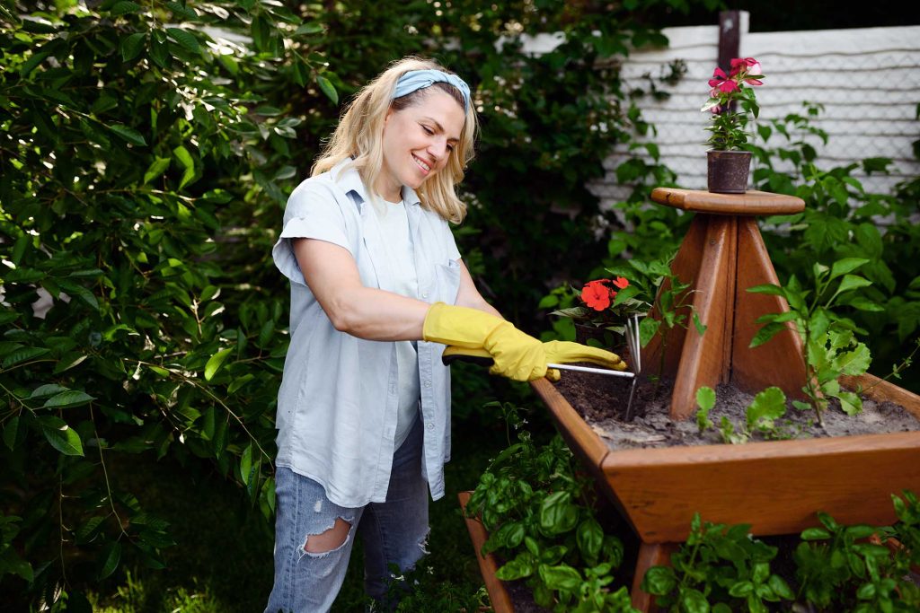Woman with hoe at the flowerbed in the garden. Female gardener takes care of plants outdoor, gardening hobby, florist lifestyle and leisure
