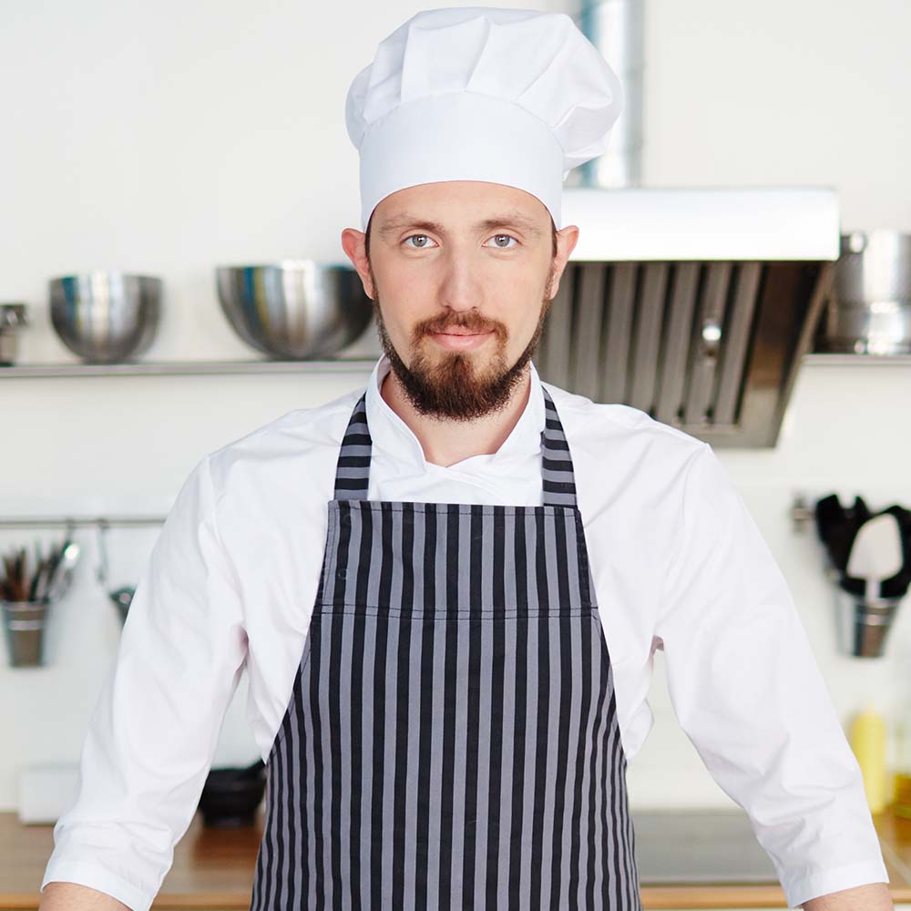 Pastry chef in uniform standing by his workplace
