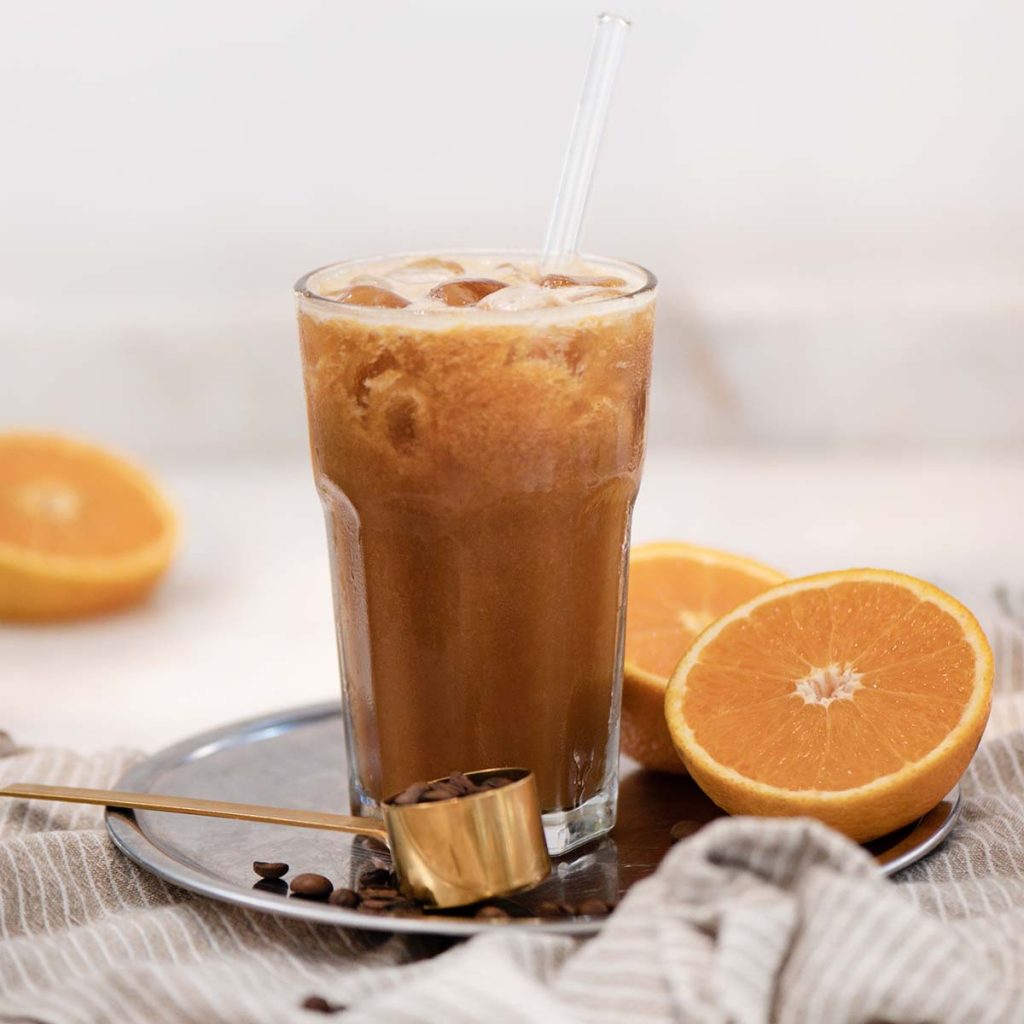 Iced Coffee and fresh ripe orange juice blended beverage drink with fresh ingredients over white background, close-up, selective focus. Idyllic drink for breakfast concept