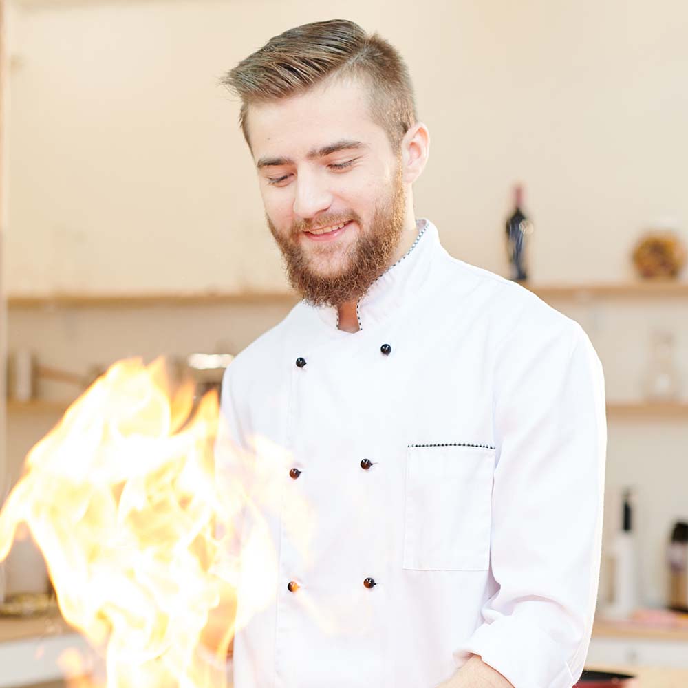 Waist up portrait of smiling  professional chef working in modern restaurant kitchen standing at wooden table and cooking flambe dish, copy space