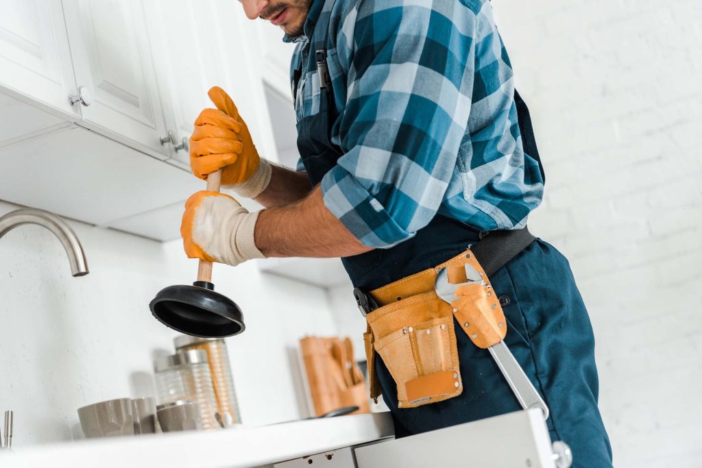 cropped view of handyman with tool belt holding plunger in kitchen