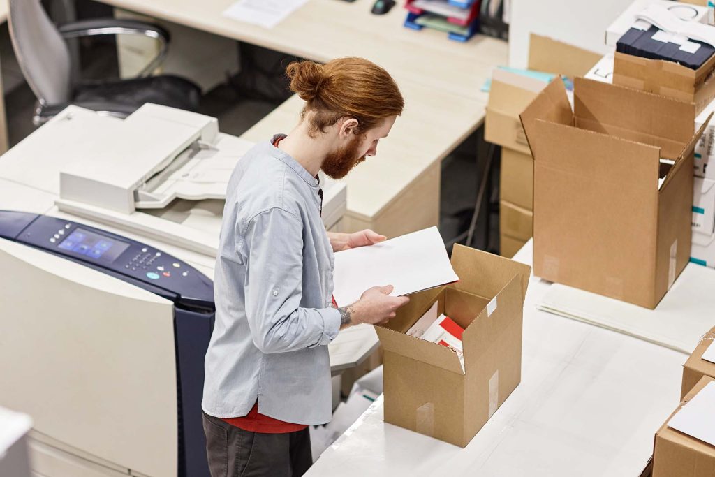High angle portrait of young man packaging print products in publishing shop, copy space