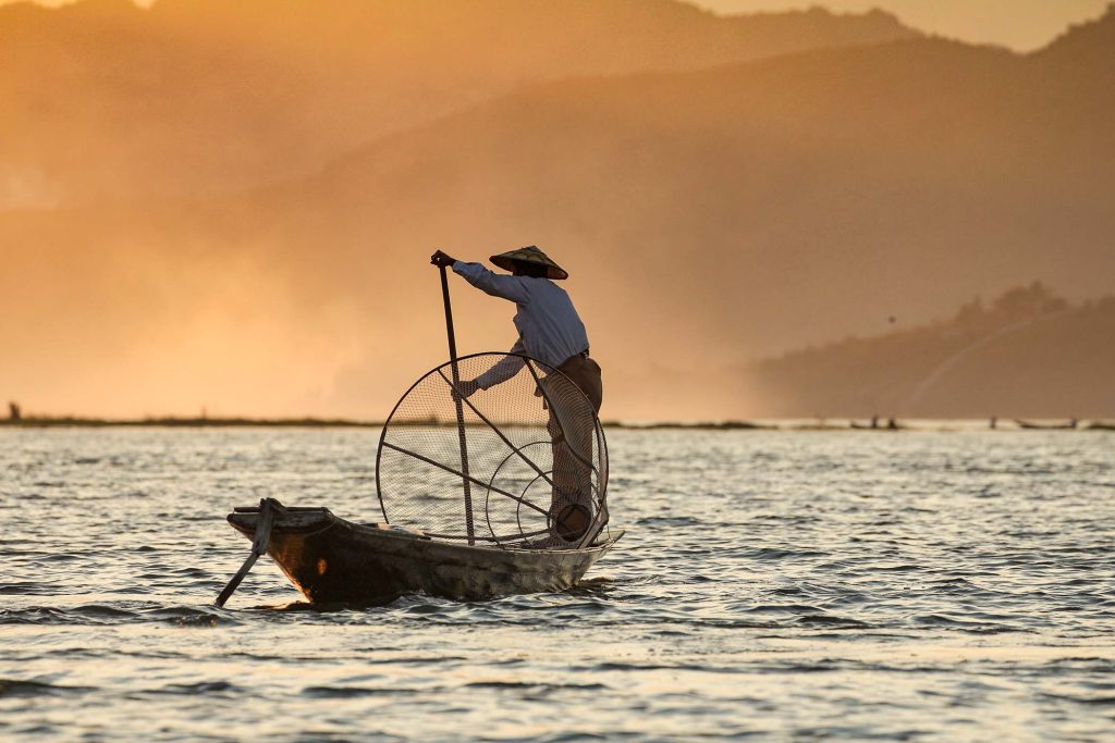 Asian fisherman on boat at sunset