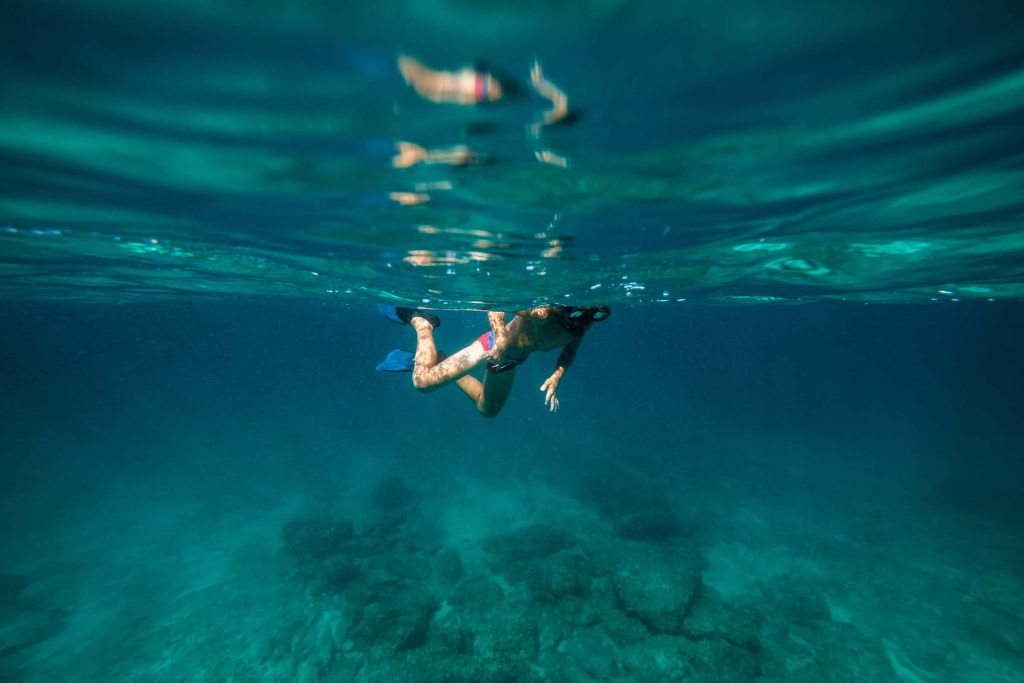 Full body of unrecognizable boy in snorkeling mask and flippers swimming in deep blue seawater near bottom with coral reef