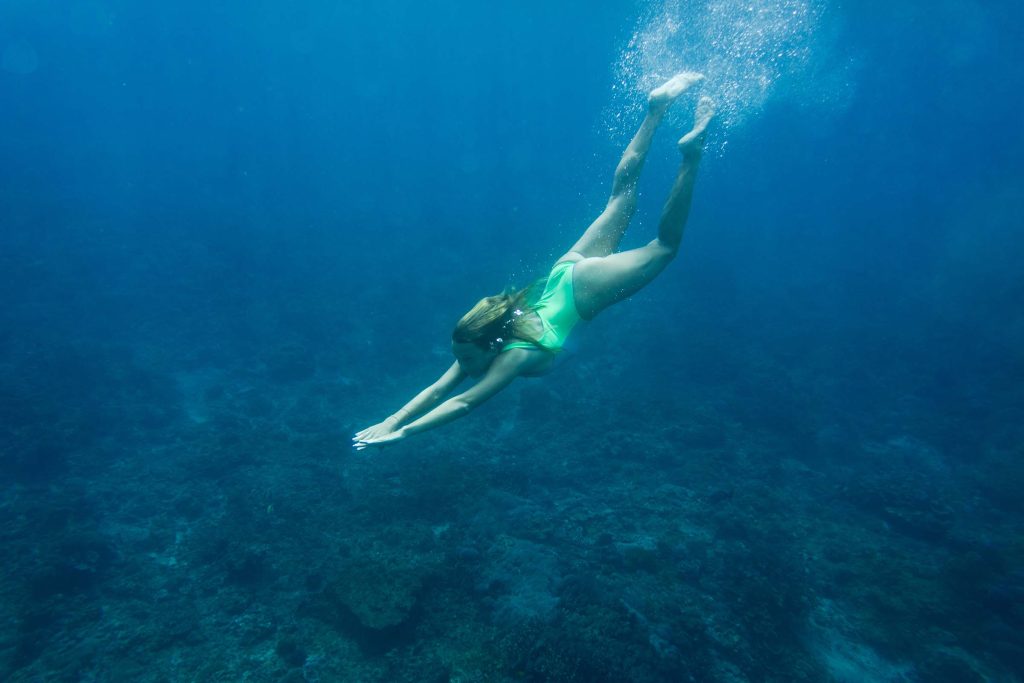 underwater photo of young woman in swimming suit diving in ocean alone