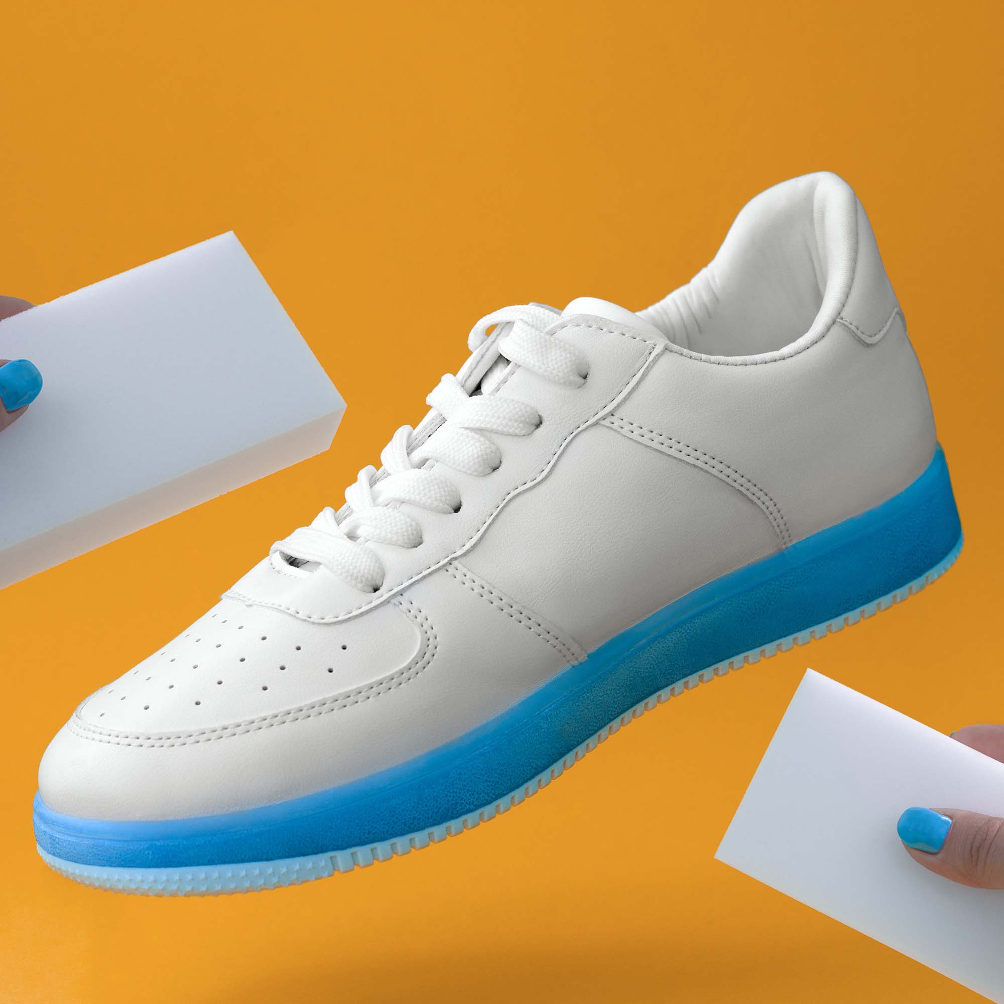 trendy white sneakers with blue sole  and female hands with sponges  on a yellow background , shoes care concept