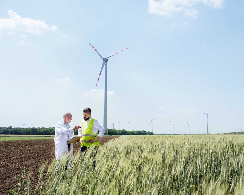 Two engineers or technicians with clipboard standing on wind farm, making notes.