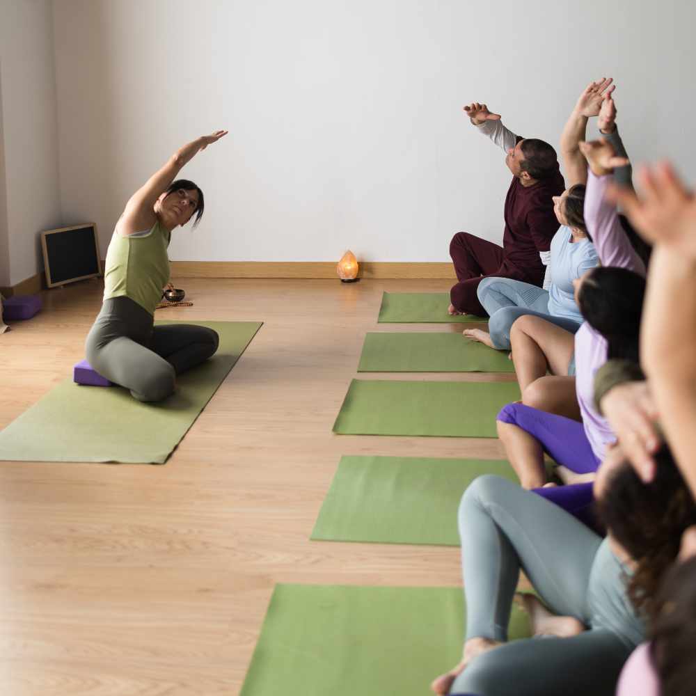 Diverse group of people sitting on green mats, stretching during a focused vinyasa yoga class in a wellness studio