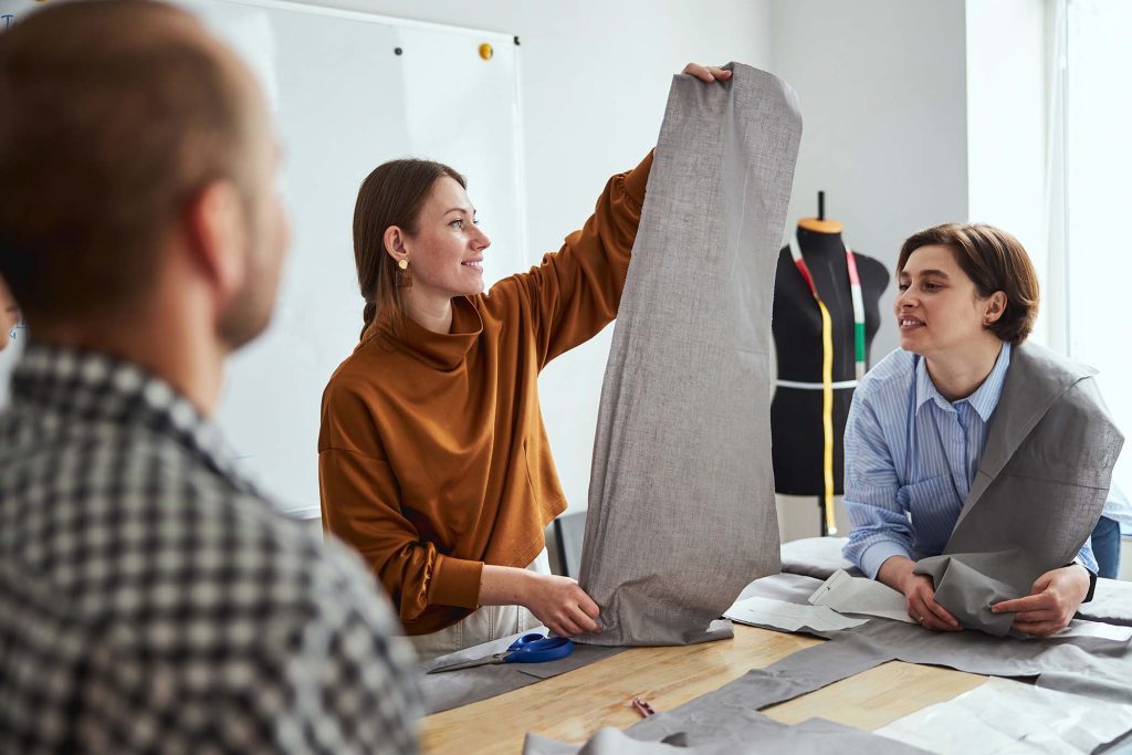 Woman smiling while keeping a piece of fabric from both ends above the table near a man and female coworker