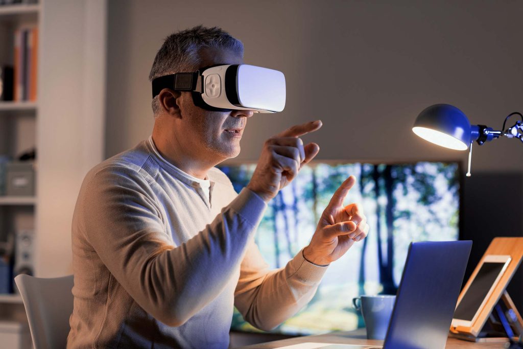 Man sitting at desk at home and experiencing virtual reality, he is wearing a VR headset and interacting with virtual screens