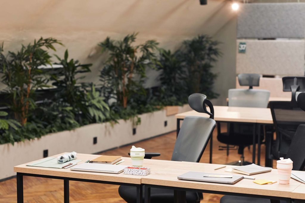 Background image of modern open space office decorated with plants, focus on workplace with wooden table and ergonomic chair in foreground, copy space