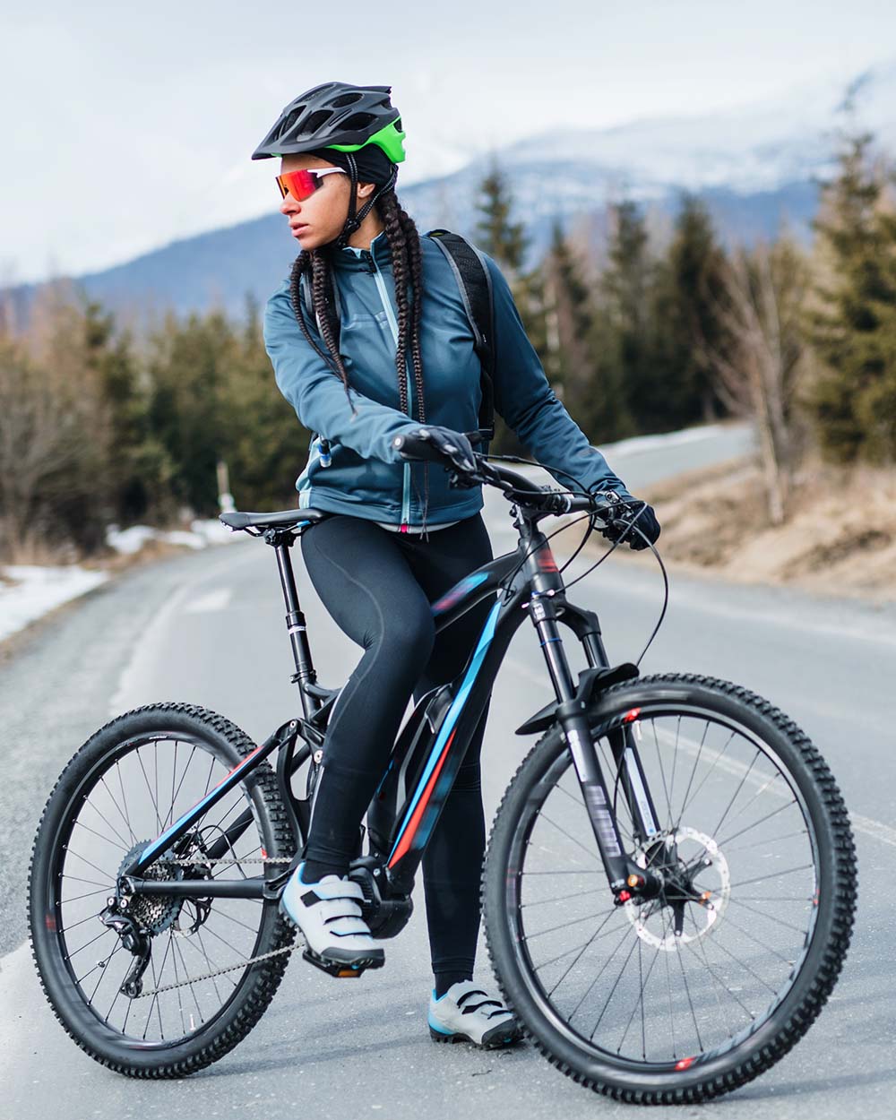 A female mountain biker standing on road outdoors in winter nature. Copy space.