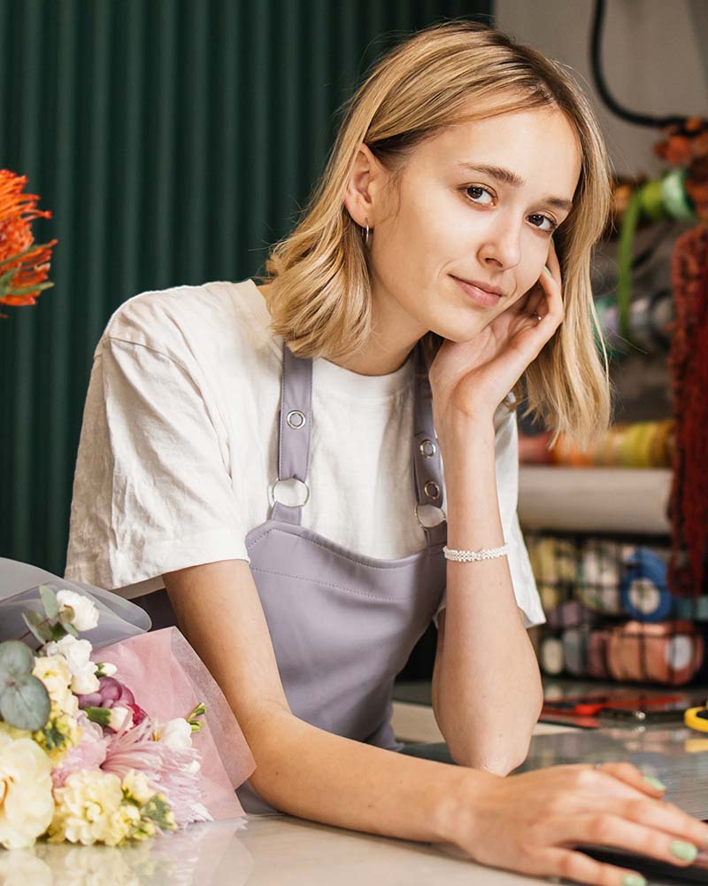 Portrait of attractive woman florist working on tablet at workplace. Concentrated female sitting at counter in floral store and typing on digital tablet.