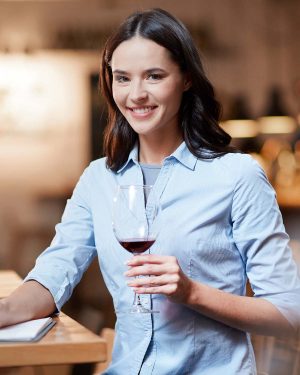 Smiling businesswoman holding a glass of red wine and making notes